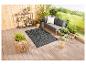 Un tapis tissé noir et blanc sur une terrasse en bois avec un salon de jardin gris.