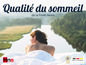 Une femme allongée sur un drap blanc avec vue sur un lac et le logo 'Hna Schlafsysteme' avec 'Geprüfte Qualität'
