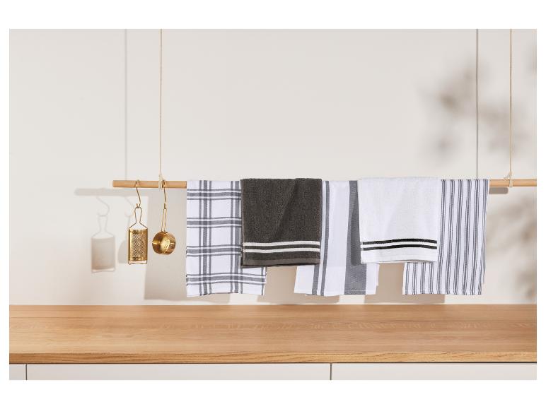 Torchons de cuisine assortis suspendus à une barre en bois, avec des ustensiles de cuisine dorés.