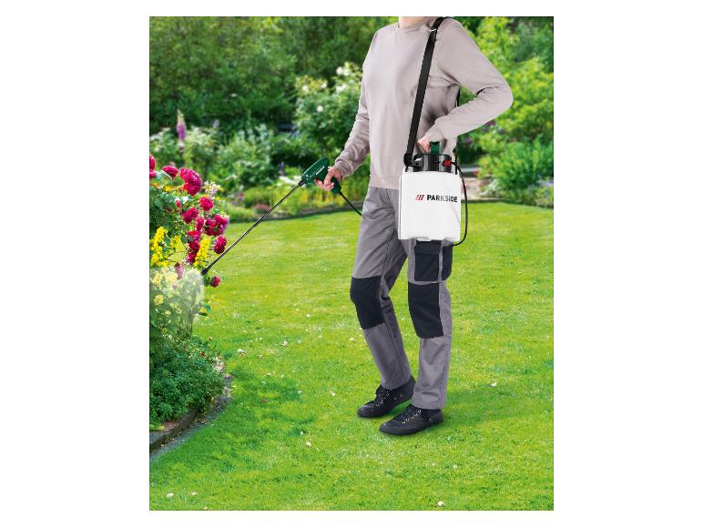 Personne utilisant un pulvérisateur à pression PARKSIDE dans un jardin fleuri.