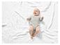 Un bébé dans une combinaison grise sur une couverture blanche.