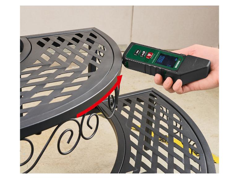 Une main tient un télémètre laser Parkside contre une étagère en métal noir.