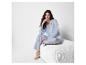 Une femme en pyjama rayé assise sur un lit blanc.