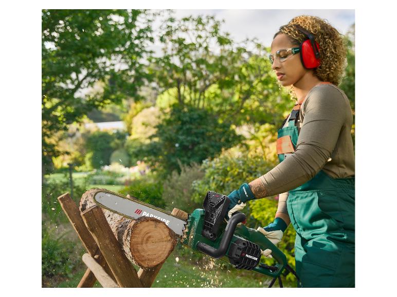 Femme en équipement de sécurité coupant du bois avec une tronçonneuse Parkside dans un jardin.