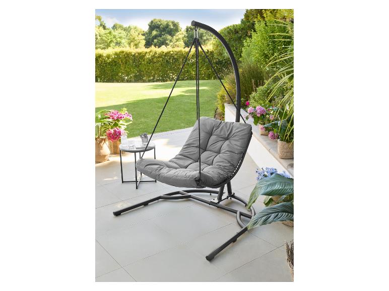 Fauteuil suspendu œuf gris avec une table d'appoint sur une terrasse avec des plantes de jardin.