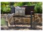 Banc de jardin avec coussins et plaid, sur fond de verdure et mur en pierre.
