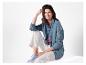 Une femme porte une veste en jean, un pantalon blanc et des baskets bleues.