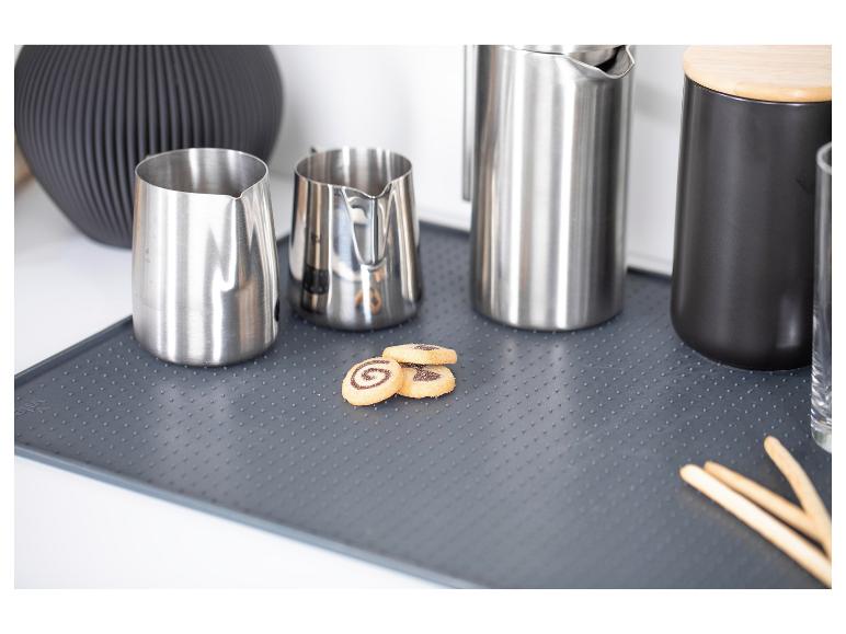 Ustensiles de cuisine en acier inoxydable et pot noir sur un tapis de séchage avec des biscuits.