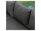 Détail d'un canapé en tissu gris foncé avec coussins, sur fond vert flou.