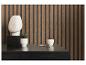 Commode noire avec sculpture blanche, plante et tasse devant un mur à lattes en bois.
