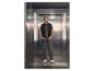 Homme en gilet dans un ascenseur, portant un jean et un t-shirt.