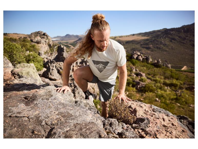 Homme en t-shirt et short de sport escaladant des rochers en montagne.