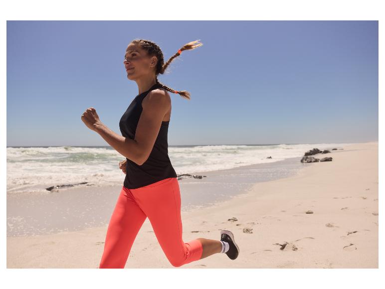Femme courant en leggings et débardeur sur une plage.