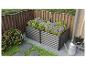Carrés potagers surélevés gris avec plantes fleuries dans un jardin avec clôture en bois.