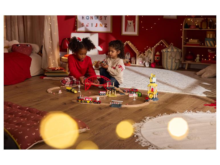 Deux enfants jouent avec un train en bois dans une pièce festive.