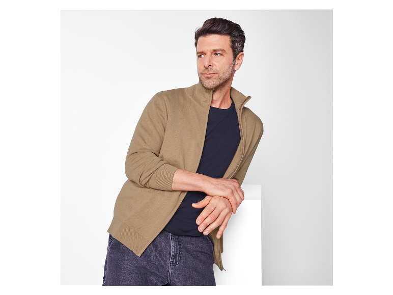 Un homme pose en portant un cardigan beige zippé.