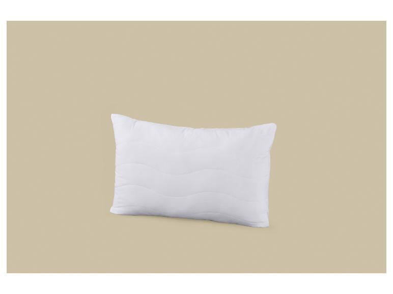 Oreiller blanc avec un motif ondulé sur fond beige.