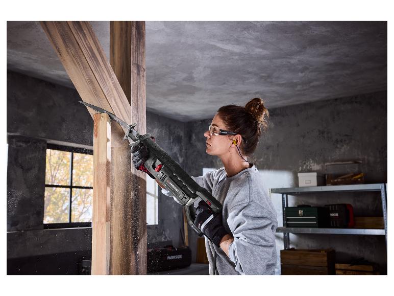 Femme utilisant une scie sabre Parkside pour couper du bois, portant des lunettes de sécurité et des bouchons d'oreille.