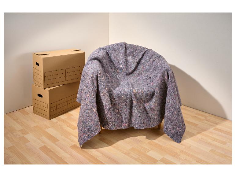 Cartons de déménagement empilés à côté d'une chaise recouverte d'une couverture de protection.