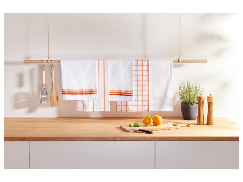 Des torchons de cuisine à rayures et à carreaux oranges accrochés à un support en bois.