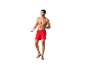 Un homme en short de bain rouge tient un ballon de volley blanc.