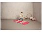 Une fille se tient sur un tapis de gymnastique rose avec un cerceau en arrière-plan.