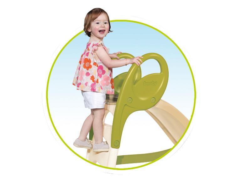 Enfant souriant grimpant sur un toboggan vert.