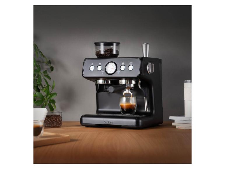 Machine à expresso noire avec grains de café et un verre d'expresso sur une table en bois.
