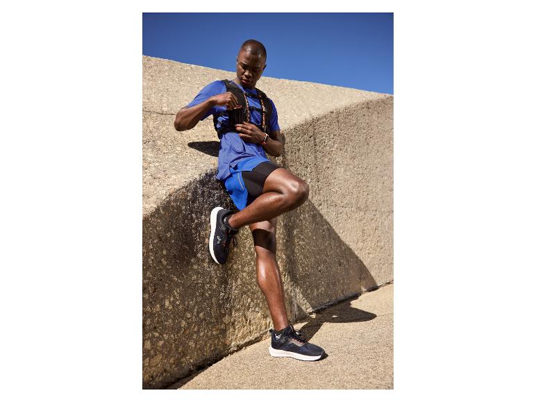 Homme en tenue de sport bleue et gilet de course appuyé contre un mur en béton.