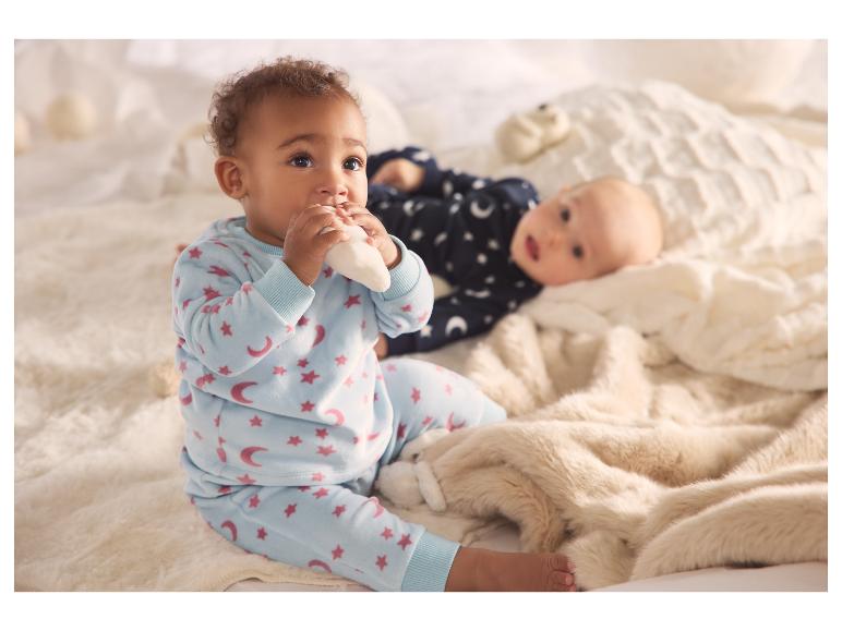 Deux bébés en pyjamas doux, l'un assis et l'autre allongé sur une couverture moelleuse.