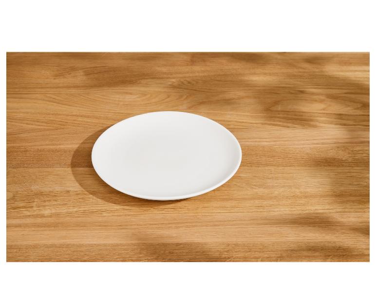 Assiette blanche vide sur une table en bois avec des ombres de feuilles