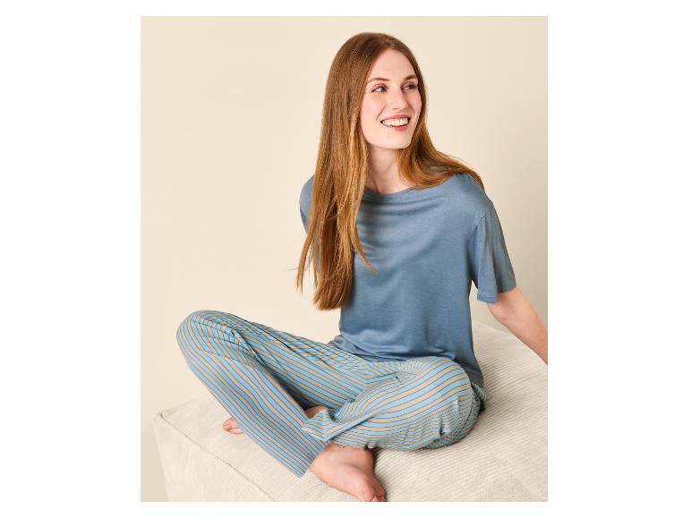 Femme en haut de pyjama bleu et pantalon rayé assise sur un canapé.