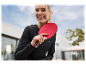 Une femme souriante tient une raquette de ping-pong rouge.