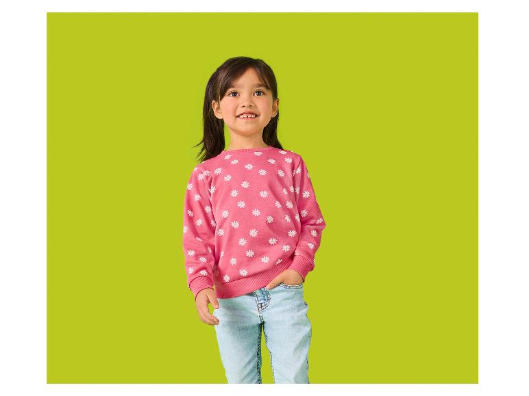 Petite fille souriante en pull rose à fleurs et jean bleu clair