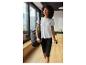 Femme en t-shirt de sport blanc et legging noir, portant un sac de sport et une bouteille d'eau.