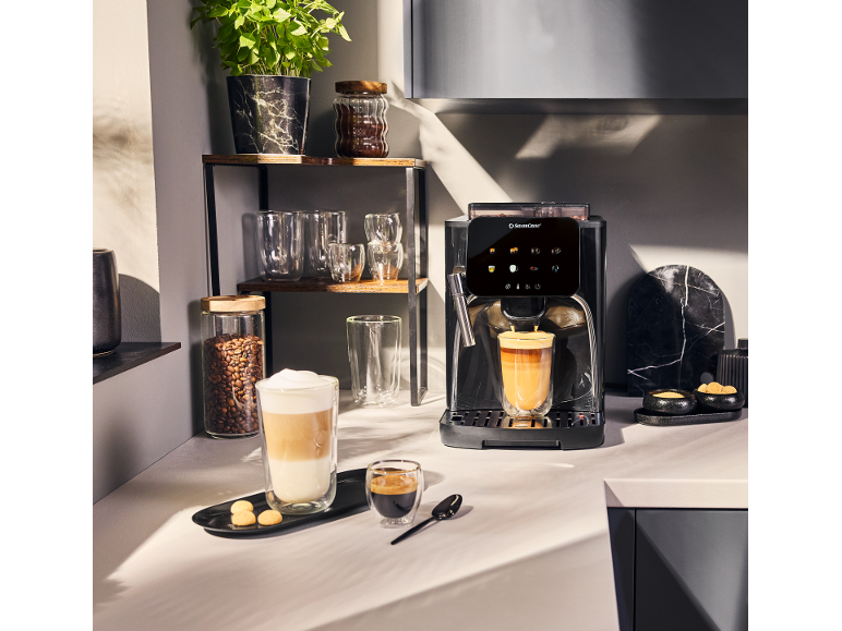 Machine à café avec deux tasses de café, des grains de café et une plante dans la cuisine.