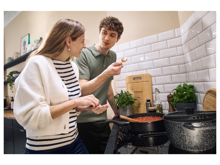 Un couple en cuisine prépare une sauce tomate dans une casserole.