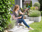 Une femme assise sur une terrasse avec des outils de jardin Gardena.