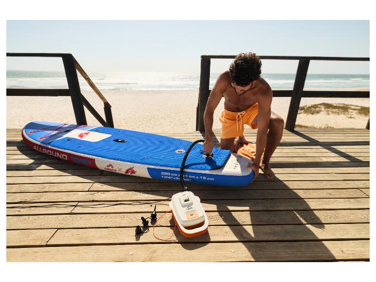 Homme gonflant une planche de SUP CRIVIT sur la plage avec une pompe électrique.