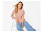 Femme en t-shirt rose et jean assise sur une chaise blanche.