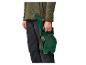 Homme en veste verte et pantalon foncé tenant un tuyau d'arrosage avec enrouleur.