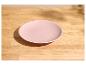 Assiette rose pâle sur une table en bois clair avec des ombres