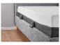 Un lit gris avec un matelas et des pieds en bois.