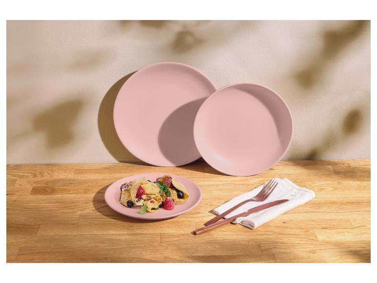 Assiettes rose pastel avec crêpes aux fruits et couverts en cuivre sur une table en bois.
