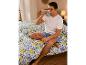 Homme buvant dans une tasse, assis sur un lit avec linge de lit citron.
