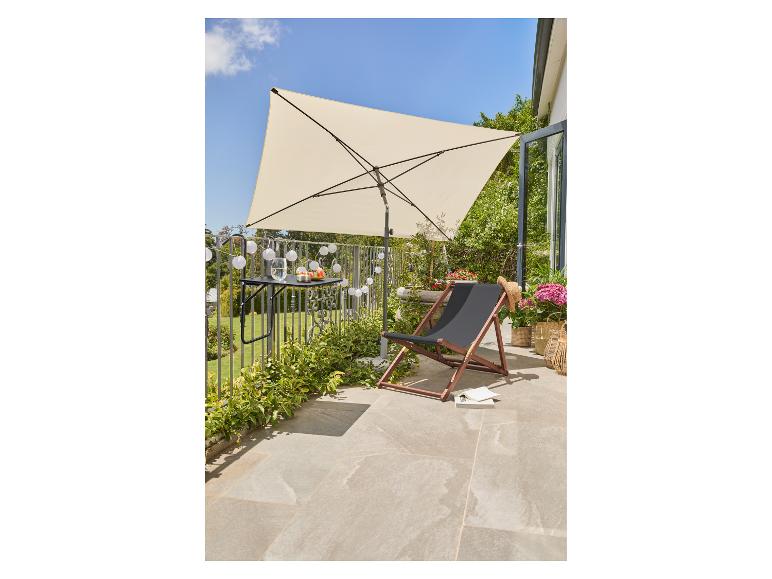 Balcon avec un parasol crème, une chaise longue noire et une petite table avec des collations.