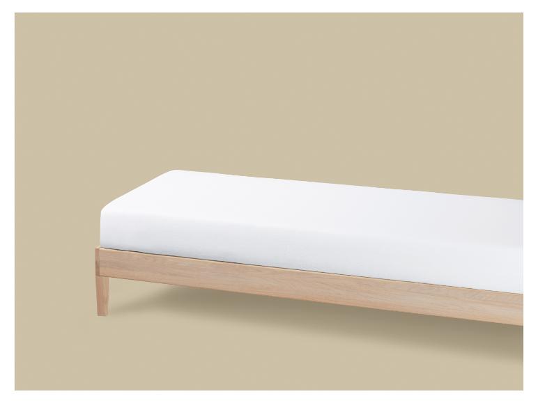 Un lit simple en bois clair avec un matelas blanc sur fond beige.
