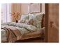 Chambre à coucher avec parure de lit verte à motifs, plaid beige et cadre de lit en bois.