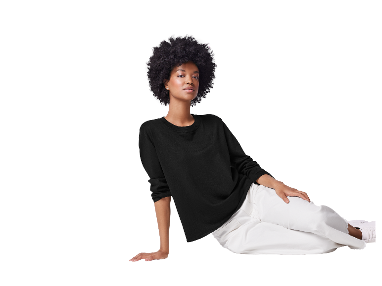 Modèle avec de grands cheveux afro pose avec un pull noir et un pantalon blanc.