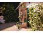 Outils de jardinage suspendus à une porte en bois, avec une pelle et un râteau au premier plan.